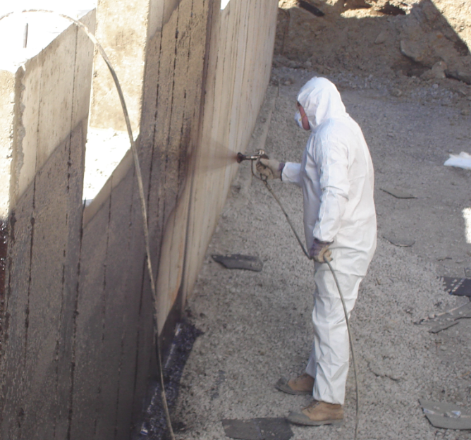 SafeStep technician spray-applying TUFF-N-DRI waterproofing membrane to a new home foundation wall
